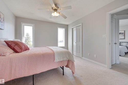 This room features light-colored walls, two windows providing natural light, a ceiling fan with integrated lighting, and carpeted flooring - 24 Birchmont Drive, Leduc, AB - Indoor Photo Showing Bedroom
