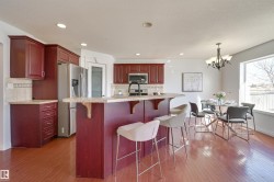 The kitchen features dark wood cabinetry, stainless steel appliances, and a breakfast bar with a light-colored countertop - 
