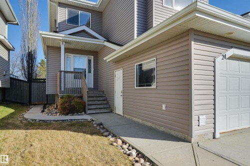 Exterior featuring tan horizontal siding, a white garage door, and an inviting front porch with wooden railings and steps - 24 Birchmont Drive, Leduc, AB - Outdoor