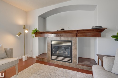 Living area featuring hardwood flooring, a fireplace with a tiled surround, a decorative wood mantel, and an arched wall niche - 24 Birchmont Drive, Leduc, AB - Indoor Photo Showing Living Room With Fireplace