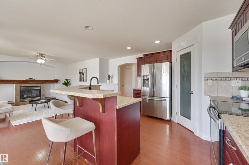The kitchen features wood flooring, a stainless steel refrigerator, and a kitchen island with a stone countertop - 24 Birchmont Drive, Leduc, AB - Indoor Photo Showing Kitchen With Fireplace With Stainless Steel Kitchen With Upgraded Kitchen