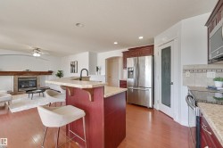 The kitchen features wood flooring, a stainless steel refrigerator, and a kitchen island with a stone countertop - 