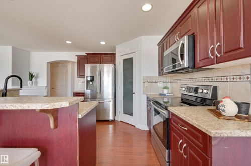 The kitchen features rich red cabinetry, stainless steel appliances, and light-colored countertops - 24 Birchmont Drive, Leduc, AB - Indoor Photo Showing Kitchen With Stainless Steel Kitchen With Upgraded Kitchen