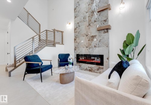 Two-story living area featuring a full-height stone-clad fireplace with an integrated linear electric insert, contemporary wood and metal railing staircase, and recessed ceiling lighting - 4727 17 Avenue Sw, Edmonton, AB - Indoor With Fireplace