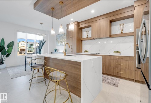 Gourmet kitchen featuring a waterfall island with a white stone-finish countertop, wood-finish cabinetry, integrated appliances, a white stone-finish backsplash, and pendant lighting - 4727 17 Avenue Sw, Edmonton, AB - Indoor Photo Showing Kitchen With Upgraded Kitchen