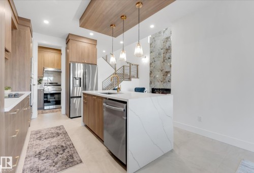 Kitchen featuring a waterfall island with stone countertop, stainless steel appliances, wood-finish cabinetry, and a wood-paneled ceiling accent - 4727 17 Avenue Sw, Edmonton, AB - Indoor Photo Showing Kitchen With Upgraded Kitchen