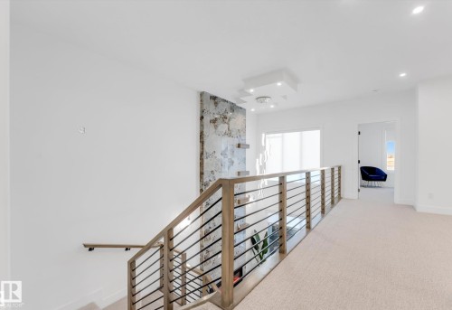 Upper-level landing featuring a modern horizontal metal railing system with wood-finish top rail, recessed lighting, and a textured accent wall - 4727 17 Avenue Sw, Edmonton, AB - Indoor Photo Showing Other Room