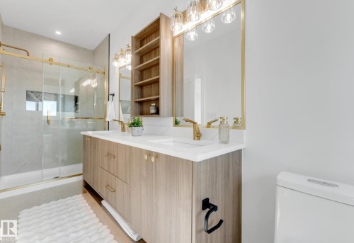 Bathroom featuring a dual-sink vanity with wood-finish cabinetry, white countertops, and gold-finish fixtures - 4727 17 Avenue Sw, Edmonton, AB - Indoor Photo Showing Bathroom