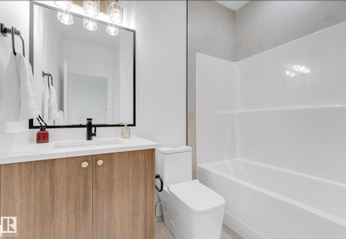 Bathroom featuring a wood-finish vanity with gold-tone hardware, white countertop, and rectangular sink with a matte black faucet - 4727 17 Avenue Sw, Edmonton, AB - Indoor Photo Showing Bathroom