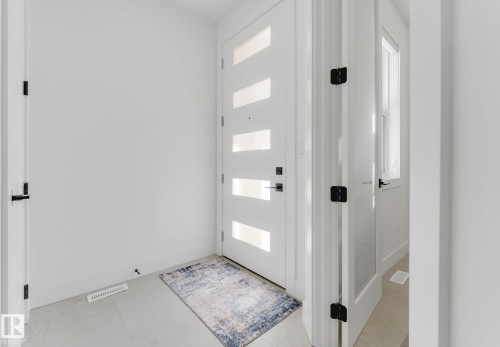 Entryway featuring a contemporary white door with frosted glass panels, black hardware, and light-toned tile flooring - 4727 17 Avenue Sw, Edmonton, AB - Indoor Photo Showing Other Room
