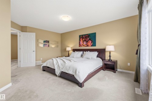 Spacious bedroom featuring light-toned carpeting, a built-in window, a white paneled door, a ceiling-mounted light fixture, and neutral wall tones - 2340 Hagen Link, Edmonton, AB - Indoor Photo Showing Bedroom