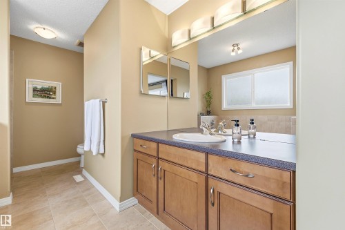 Expansive vanity with two integrated sinks and wood-finish cabinetry, illuminated by a multi-bulb light fixture - 2340 Hagen Link, Edmonton, AB - Indoor Photo Showing Bathroom