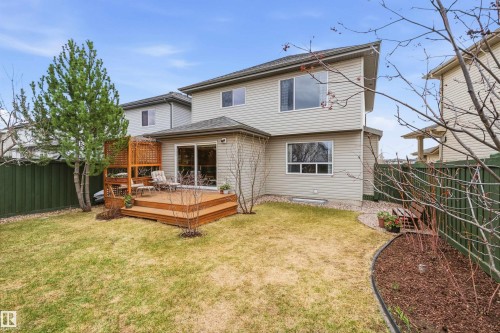 Expansive backyard featuring a multi-level wood deck, sliding glass door access, a privacy trellis, mature evergreen tree, and a green perimeter fence - 2340 Hagen Link, Edmonton, AB - Outdoor With Exterior