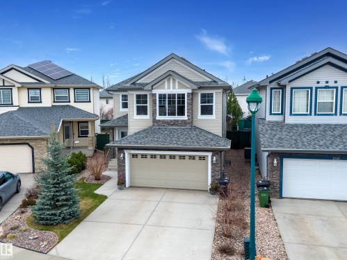 Two-story residence featuring a neutral-toned facade with stone accents, an attached two-car garage, and a concrete driveway - 2340 Hagen Link, Edmonton, AB - Outdoor With Facade