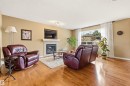 Living area featuring wood-finish flooring, a contemporary fireplace with a stone surround and mantel, and a large window with white curtains - 2340 Hagen Link, Edmonton, AB  - Indoor Photo Showing Living Room With Fireplace 
