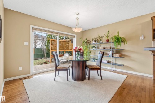 Dining area featuring wood-finish flooring, neutral wall tones, and a sliding glass door leading to an outdoor patio with a privacy screen - 2340 Hagen Link, Edmonton, AB - Indoor Photo Showing Dining Room