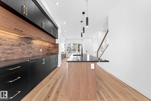 The kitchen features a large island with a dark countertop, black cabinetry with gold hardware, and a brick-style backsplash - 11021 132 Street, Edmonton, AB - Indoor Photo Showing Kitchen With Upgraded Kitchen