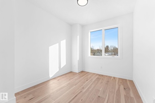 This room features light hardwood flooring, white walls, and a window providing natural light and views of trees and rooftops - 11021 132 Street, Edmonton, AB - Indoor Photo Showing Other Room