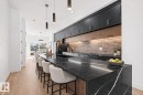 Contemporary kitchen featuring a large black stone island with white veining, undercabinet lighting, dark cabinetry with brass hardware, a dark brick-patterned backsplash, and light wood-finish flooring - 11021 132 Street, Edmonton, AB  - Indoor Photo Showing Kitchen With Upgraded Kitchen 