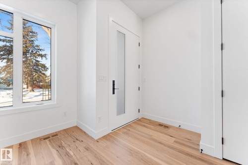 This space features light hardwood floors, white walls, and a white door with a frosted glass panel and black hardware - 11021 132 Street, Edmonton, AB - Indoor Photo Showing Other Room