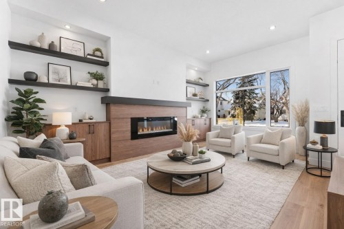 This living area features light hardwood flooring, an electric fireplace with a wood-paneled surround, and recessed lighting - 11021 132 Street, Edmonton, AB - Indoor Photo Showing Living Room With Fireplace