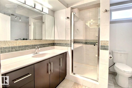 Bathroom featuring a glass-enclosed shower, a vanity with dark wood-finish cabinetry, a large integrated sink, and a rectangular mirror with integrated lighting - 9512 134 Avenue, Edmonton, AB - Indoor Photo Showing Bathroom