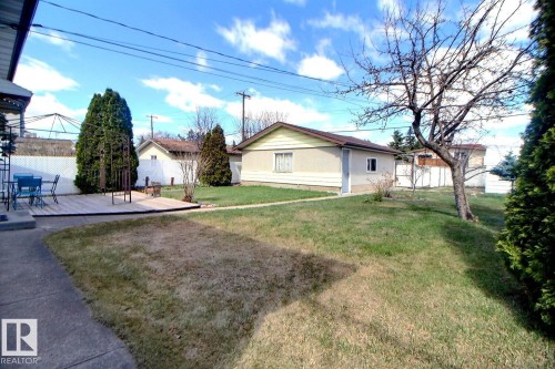 Expansive backyard featuring a wood deck, established trees, and a detached garage with siding exterior and a shingled roof - 9512 134 Avenue, Edmonton, AB - Outdoor