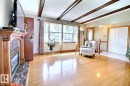 Living area featuring hardwood flooring, a fireplace with a marble-look surround, wood-beamed ceilings, and large windows - 9512 134 Avenue, Edmonton, AB  - Indoor With Fireplace 