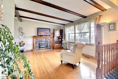 Living area featuring wood-finish flooring, a fireplace with a stone surround and wood mantel, exposed ceiling beams, and large windows - 9512 134 Avenue, Edmonton, AB - Indoor Photo Showing Living Room With Fireplace
