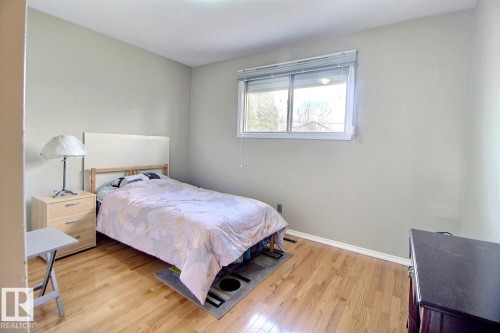 Light-filled room featuring wood-finish flooring, neutral wall paint, and a white-framed window with horizontal blinds - 9512 134 Avenue, Edmonton, AB - Indoor Photo Showing Bedroom