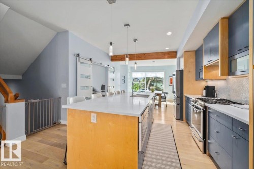 Modern kitchen featuring a large central island with seating, light wood-finish flooring, and stainless steel appliances - 11245 64 Street, Edmonton, AB - Indoor Photo Showing Kitchen With Upgraded Kitchen