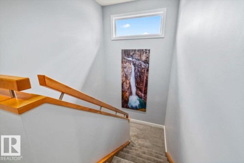 Carpeted staircase featuring light wood-finish handrails, a horizontal accent window, and neutral wall tones - 11245 64 Street, Edmonton, AB - Indoor Photo Showing Other Room