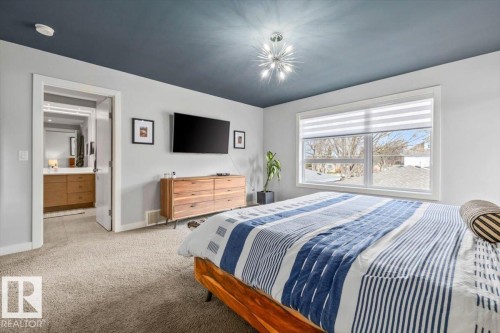 Spacious bedroom featuring light-colored carpeting, a contemporary ceiling fixture, and a large window with privacy blinds - 11245 64 Street, Edmonton, AB - Indoor Photo Showing Bedroom