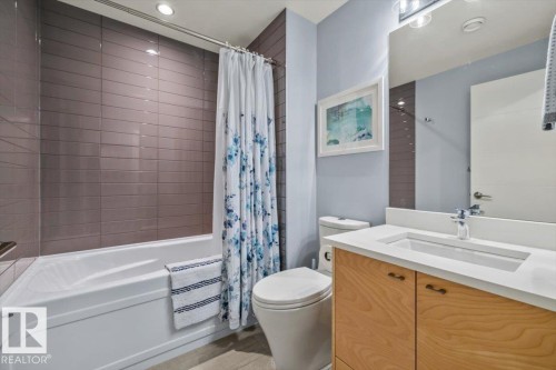 Bathroom featuring a white bathtub with subway tile surround, wood-finish vanity with an integrated sink, and an overhead vanity light fixture - 11245 64 Street, Edmonton, AB - Indoor Photo Showing Bathroom
