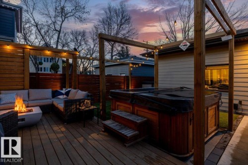 Spacious outdoor deck featuring an integrated hot tub, wood privacy fencing, a pergola structure, a concrete walkway, and an external building with a white service door - 11245 64 Street, Edmonton, AB - Outdoor With Exterior