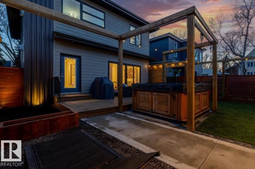 Expansive outdoor patio featuring wood-finish decking, privacy fencing, built-in hot tub, string lighting, and a fire pit - 11245 64 Street, Edmonton, AB - Indoor