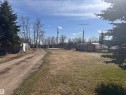 Expansive lot featuring a gravel driveway, mature evergreen trees, and a distant treeline - 5211 50 Avenue, Fawcett, AB 