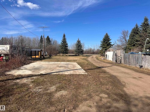 Expansive lot featuring a concrete pad, a gravel driveway, and mature evergreen trees - 5211 50 Avenue, Fawcett, AB 