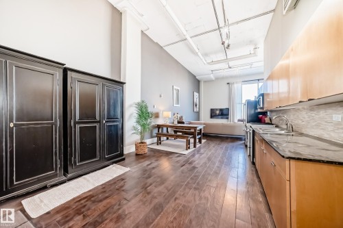 Open-concept living space with wood-finish flooring, exposed ceiling piping, recessed lighting, and a full kitchen featuring light wood cabinetry, stone countertops, and a tile backsplash - 1003 10179 105 Street Nw, Edmonton, AB - Indoor Photo Showing Kitchen With Double Sink