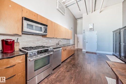 Kitchen featuring light wood-finish cabinetry, stainless steel appliances, dark stone countertops, and a tile backsplash - 1003 10179 105 Street Nw, Edmonton, AB - Indoor Photo Showing Kitchen With Double Sink