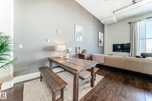 Open-concept living area featuring rich wood-finish flooring, soaring ceilings, and expansive windows with drapery - 1003 10179 105 Street Nw, Edmonton, AB - Indoor