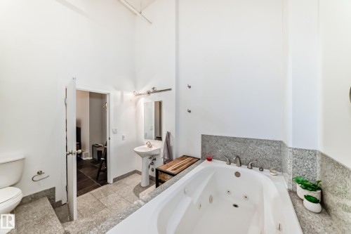 Spacious bathroom featuring a white jetted tub, a pedestal sink, and a commode - 1003 10179 105 Street Nw, Edmonton, AB - Indoor Photo Showing Bathroom