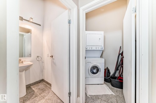 Compact laundry area featuring a stacked washer and dryer, accompanied by a powder room with a pedestal sink, wall-mounted mirror, and tile flooring - 1003 10179 105 Street Nw, Edmonton, AB - Indoor Photo Showing Laundry Room