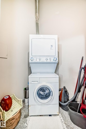 Dedicated laundry area featuring a white stacked washer and dryer unit, durable stone-finish flooring, and a visible dryer vent - 1003 10179 105 Street Nw, Edmonton, AB - Indoor Photo Showing Laundry Room