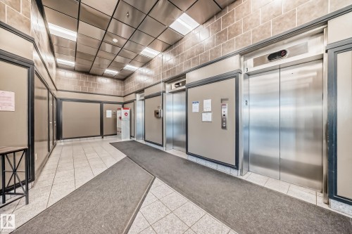 Lobby area featuring three stainless steel elevators, overhead fluorescent lighting, and a suspended metal ceiling - 1003 10179 105 Street Nw, Edmonton, AB - Indoor Photo Showing Other Room