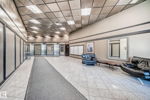 Spacious common area featuring light-toned tile flooring, recessed grid ceiling lighting, and multiple elevator access points - 1003 10179 105 Street Nw, Edmonton, AB - Indoor Photo Showing Other Room