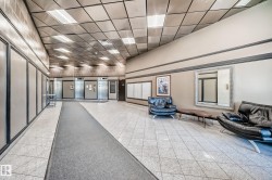 Spacious common area featuring light-toned tile flooring, recessed grid ceiling lighting, and multiple elevator access points - 