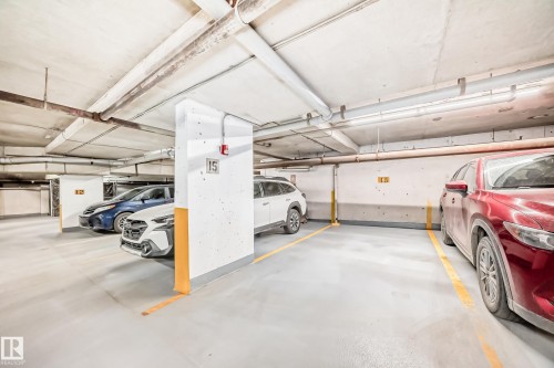 Concrete subterranean parking garage featuring exposed overhead piping, fluorescent lighting, and painted support columns - 1003 10179 105 Street Nw, Edmonton, AB - Indoor Photo Showing Garage