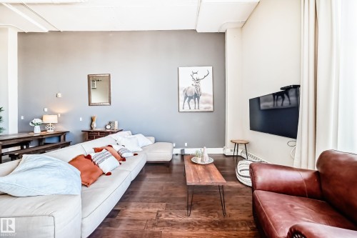 Expansive living space featuring wood-finish flooring, exposed ceiling beams, and a wall-mounted television - 1003 10179 105 Street Nw, Edmonton, AB - Indoor Photo Showing Living Room