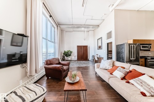Spacious open-concept living area featuring high ceilings, wood-finish flooring, a wall of large windows with white drapes, and exposed ductwork - 1003 10179 105 Street Nw, Edmonton, AB - Indoor Photo Showing Living Room